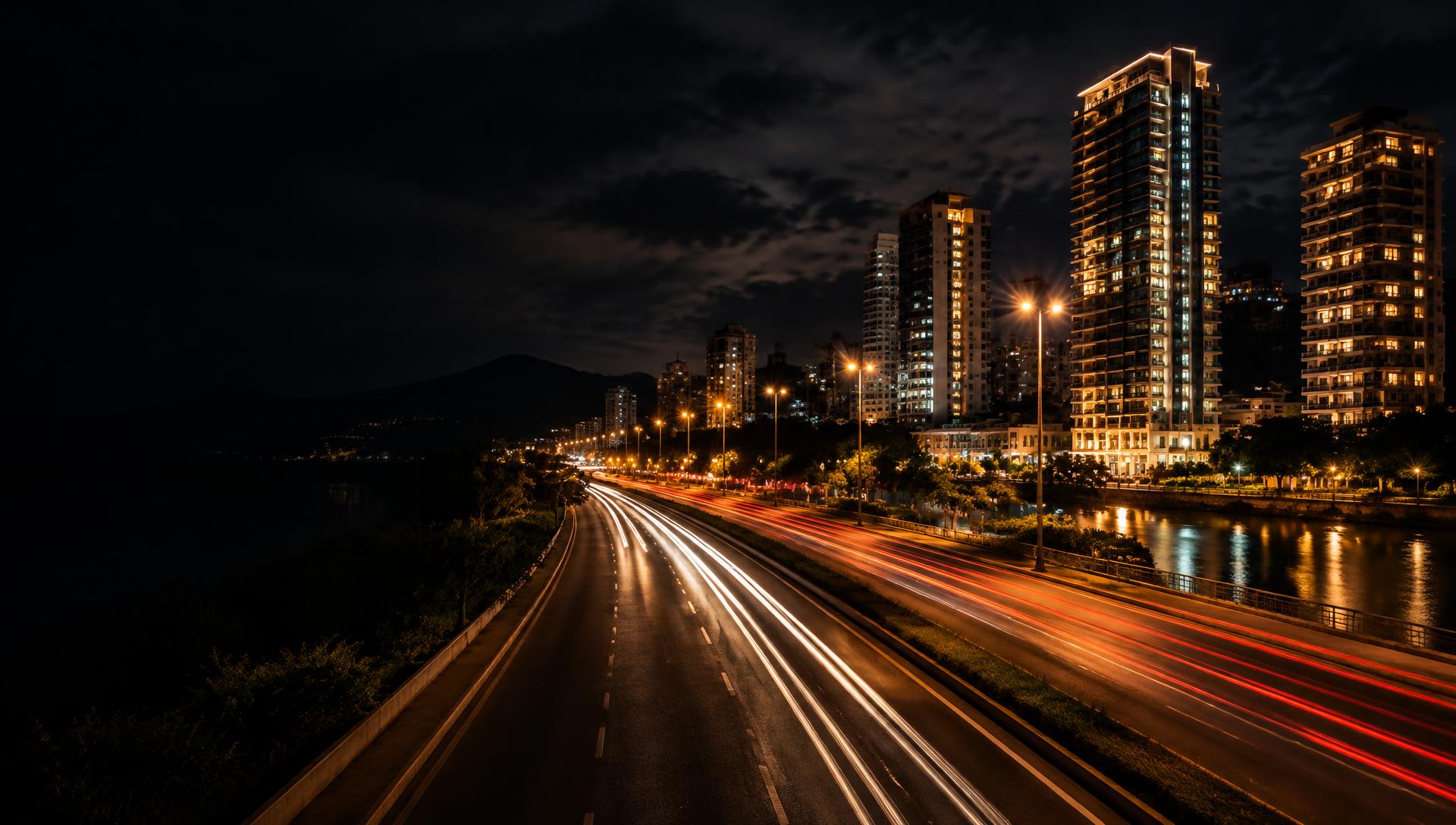 Avenida iluminada à noite, com prédios e rastros de luz dos carros